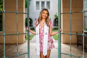 Graduate portrait session in pink floral dress under covered walkway.