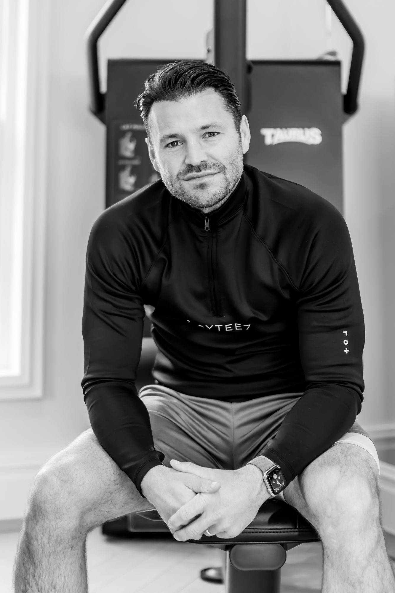 Athletic person in black workout gear seated on exercise equipment.