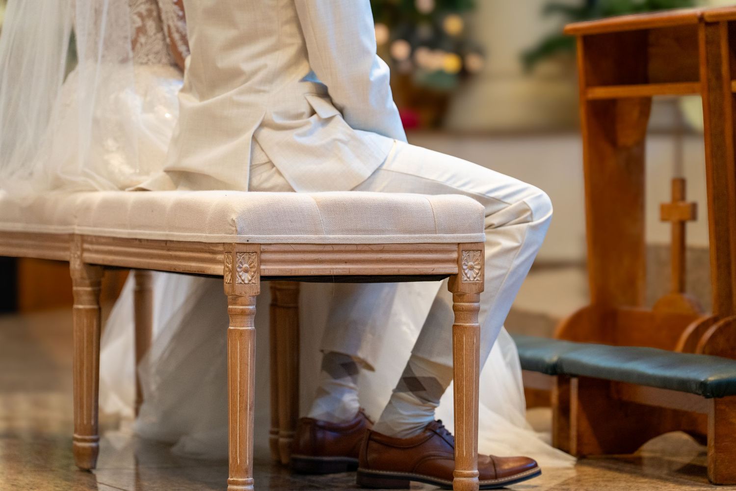 A pair of white dress shoes rests on an ornate wooden stool with a delicate white fabric draped nearby.
