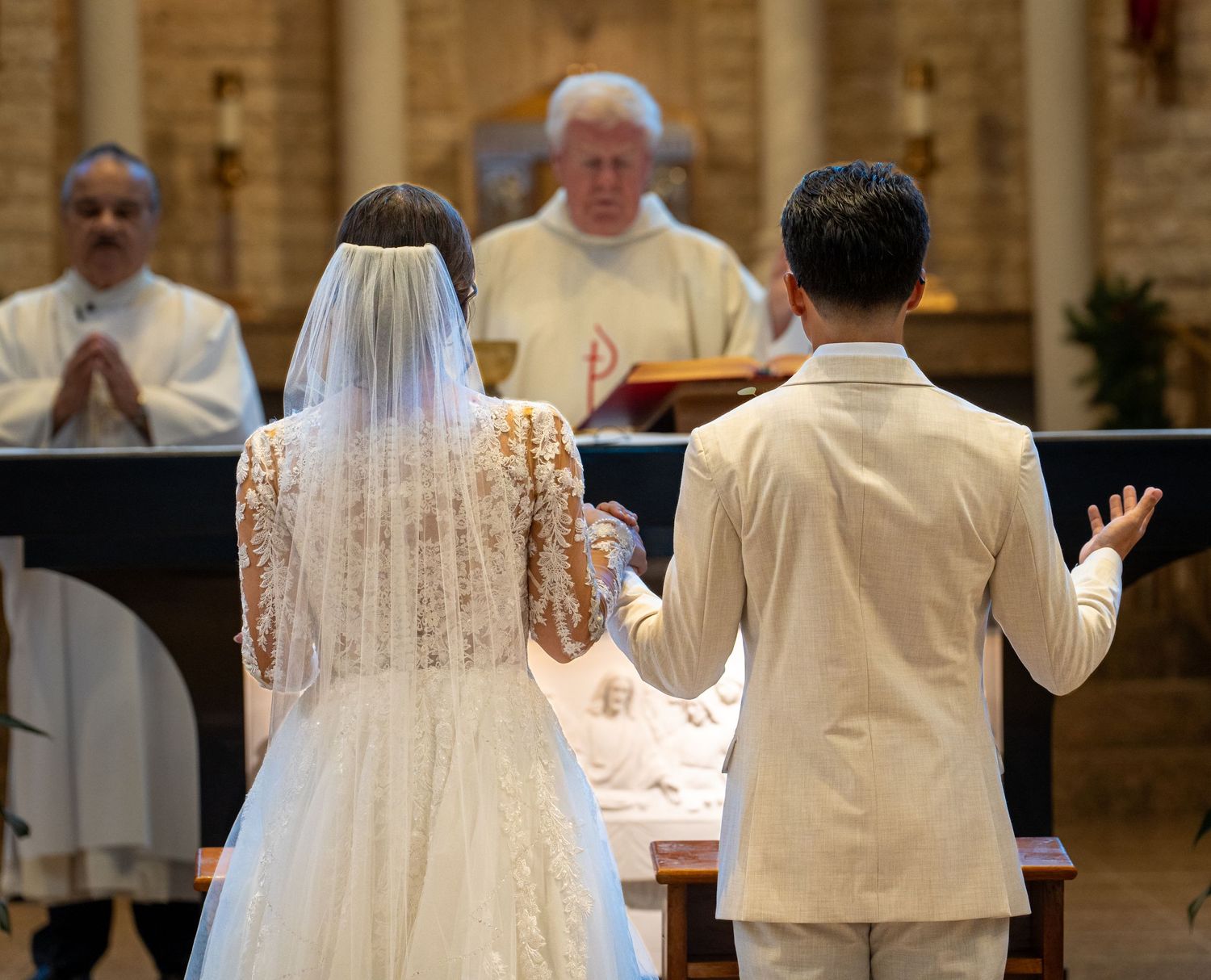 A bride and groom stand at the altar during their Catholic wedding ceremony as a priest conducts the service.