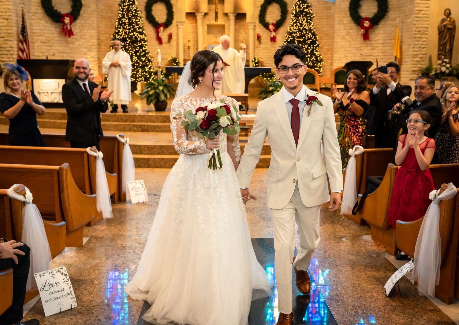 A couple walk down the church aisle after their ceremony with glowing blue lights and gold Christmas decor in the background.