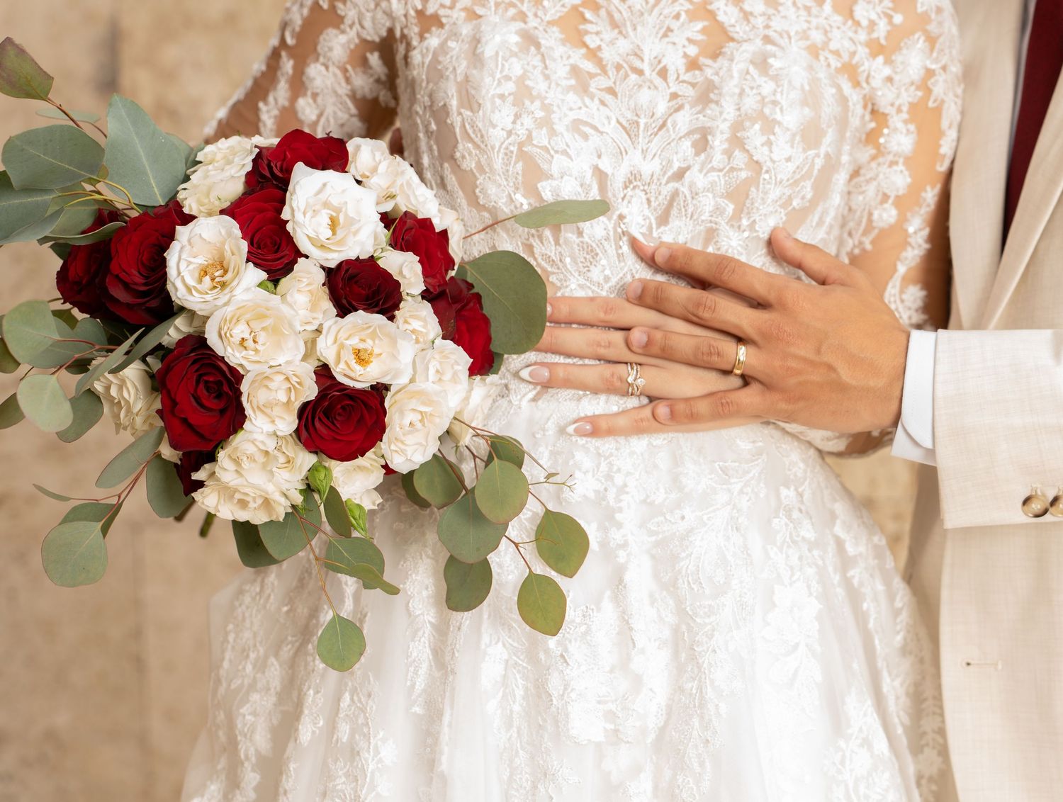 Elegant wedding bouquet with deep red and cream roses paired with eucalyptus leaves against white lace dress.