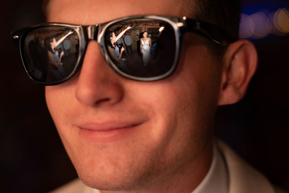 A picture of a bride in the reflection of her grooms glasses