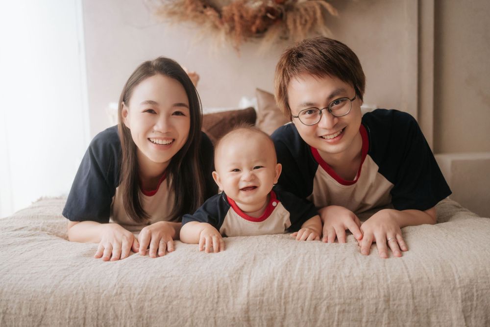 Family of three lying on bed together in casual attire.