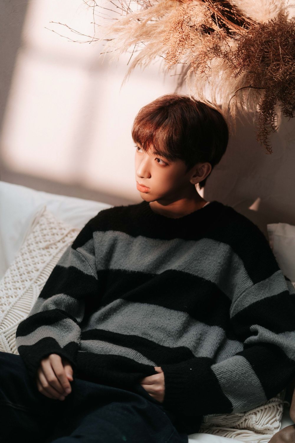 Person wearing striped sweater sitting in moody lighting with pampas grass decor.