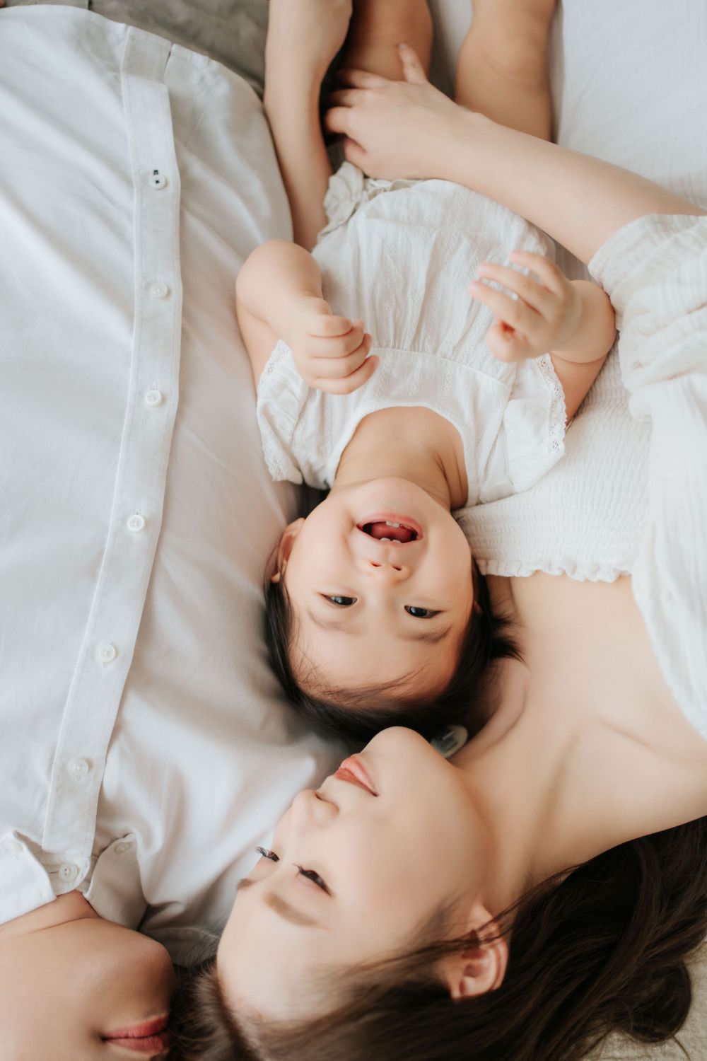 Two people lying on white bedding and smiling together.