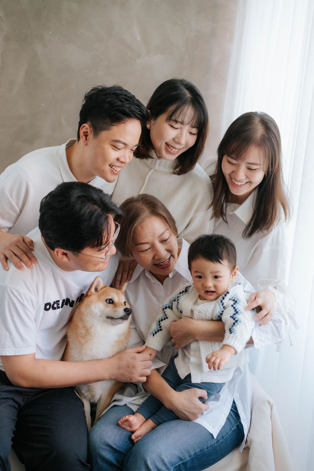 Casual family portrait with pet dog in white room setting.