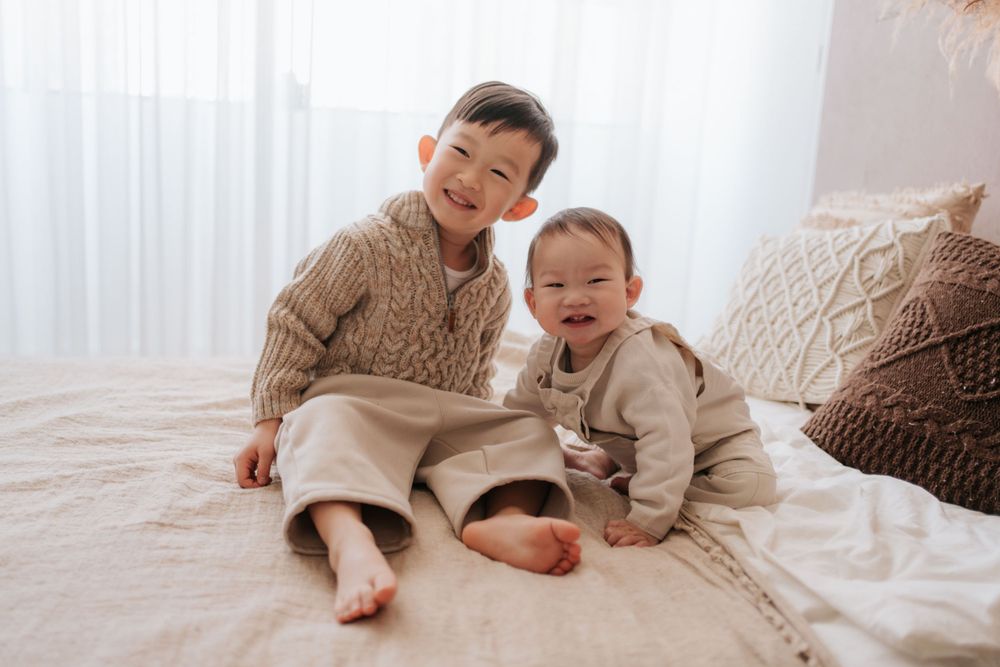 Cozy family cuddles together on a light colored bed during a lifestyle photoshoot.