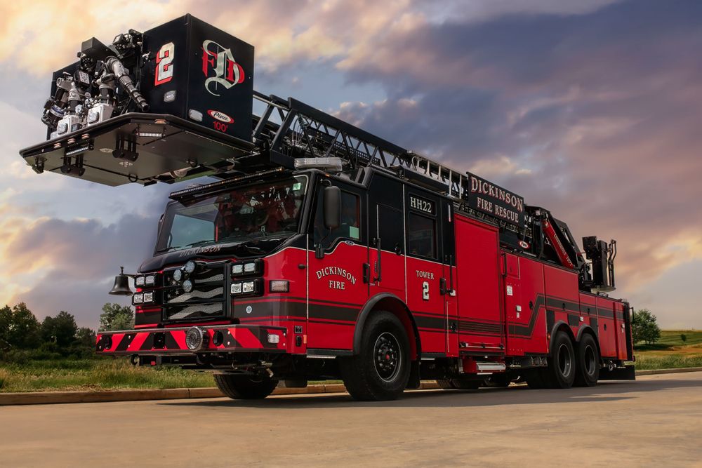 Red fire truck with extended ladder photographed against dramatic sunset sky.