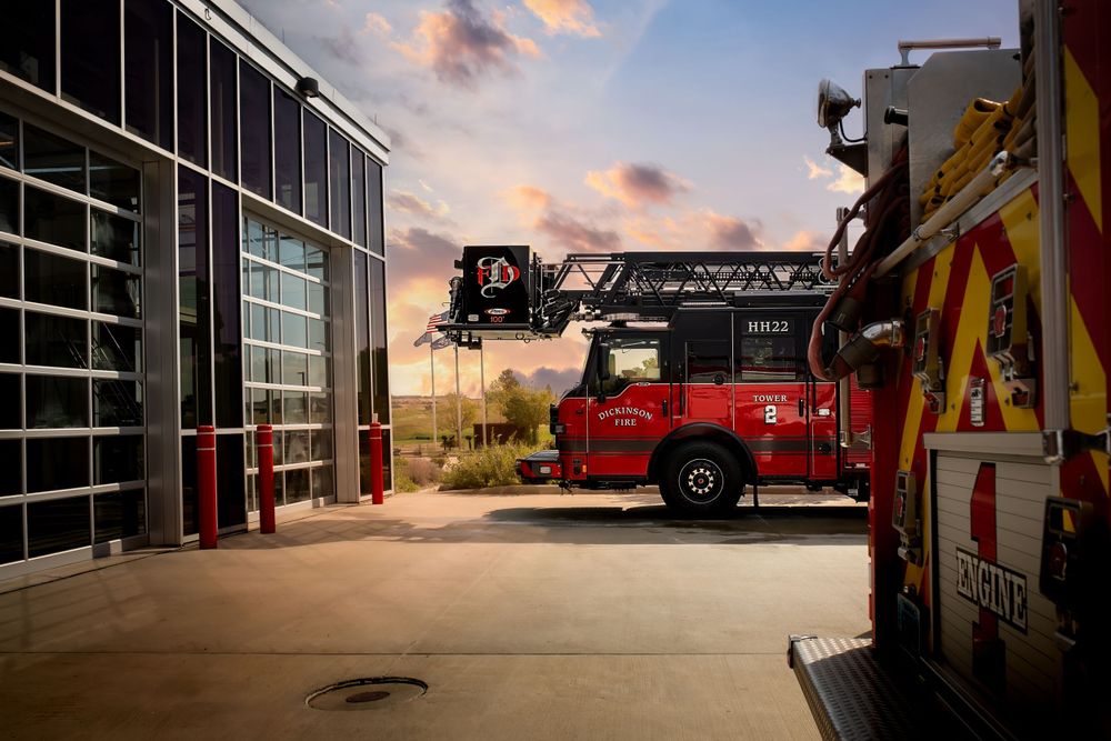 Fire station exterior with red emergency vehicles parked at sunset.