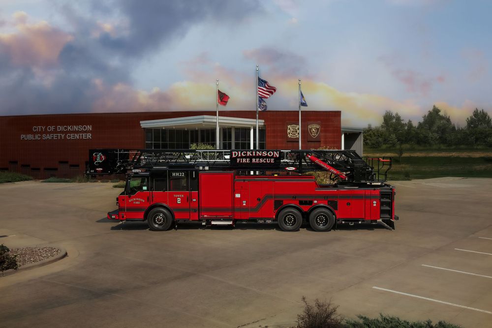 Red fire truck stationed outside brick municipal building with flags.