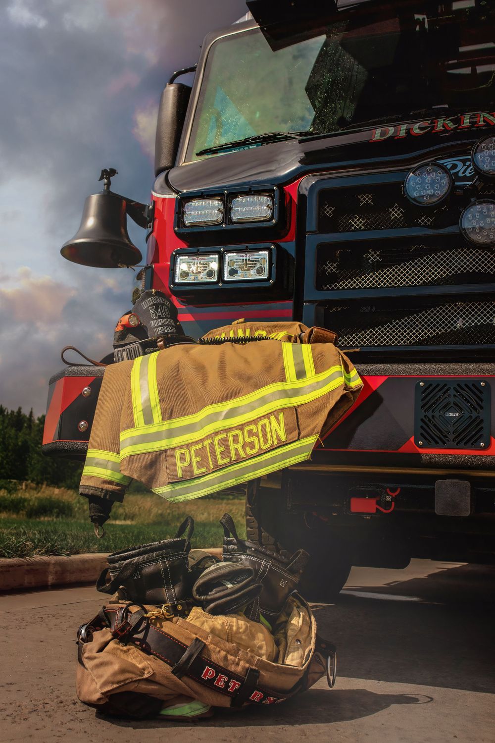 Firefighter gear and helmet displayed in front of red fire truck at dusk.