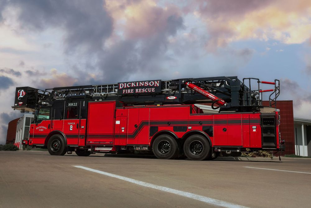 Side view of a large red Dickinson fire truck with extended ladder against cloudy sky.
