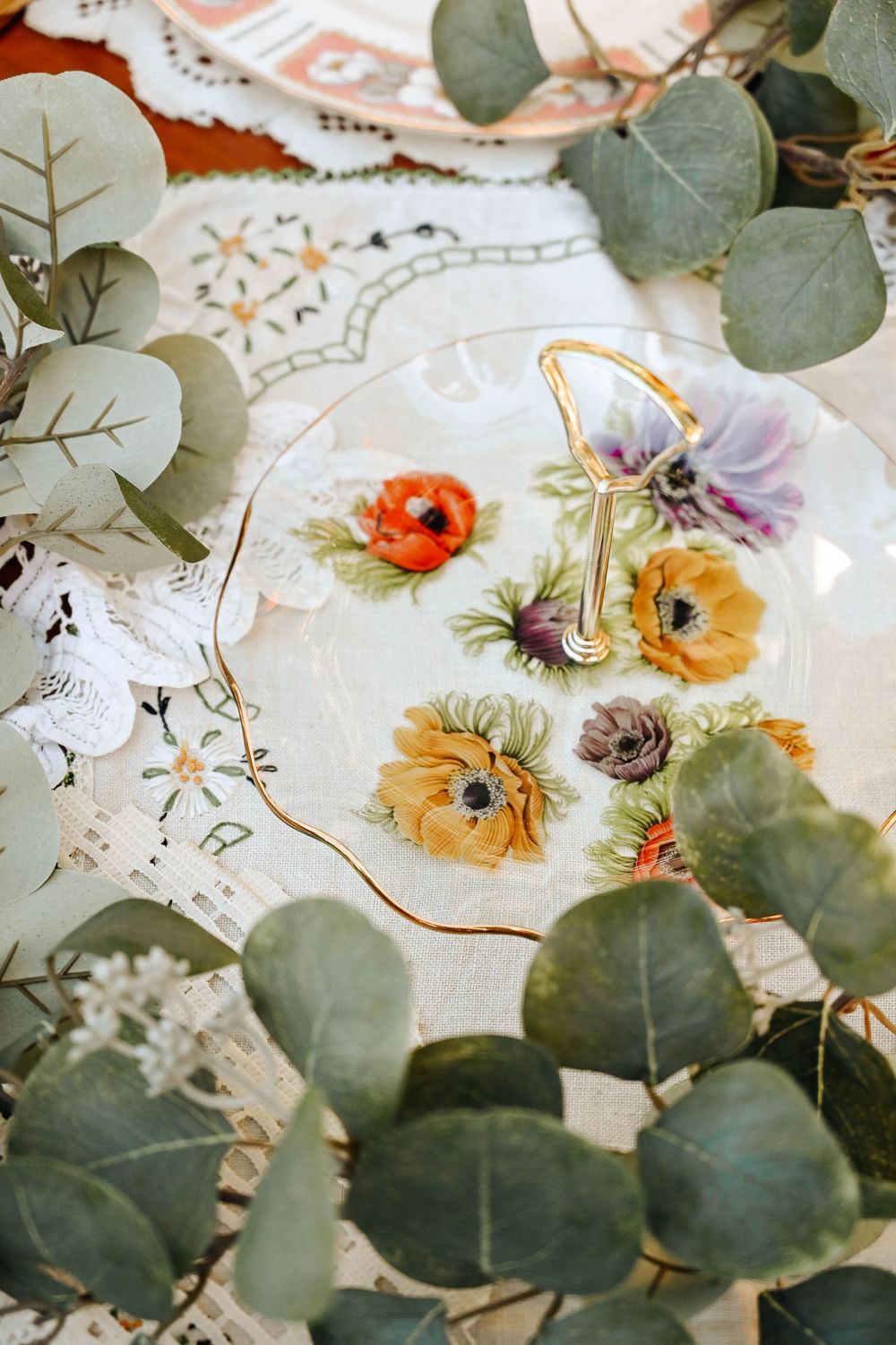 Floral wedding table setting with scattered flowers and eucalyptus leaves on cream colored fabric.