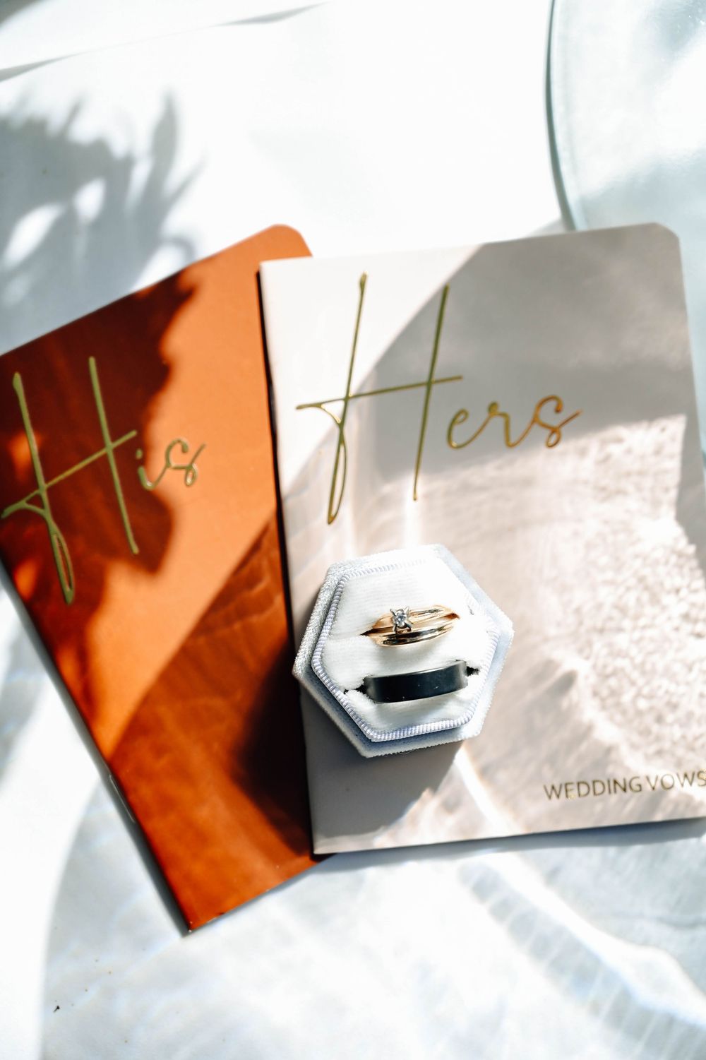 Wedding vows booklets in rose gold and white with a hexagonal ring box on white fabric in natural lighting.