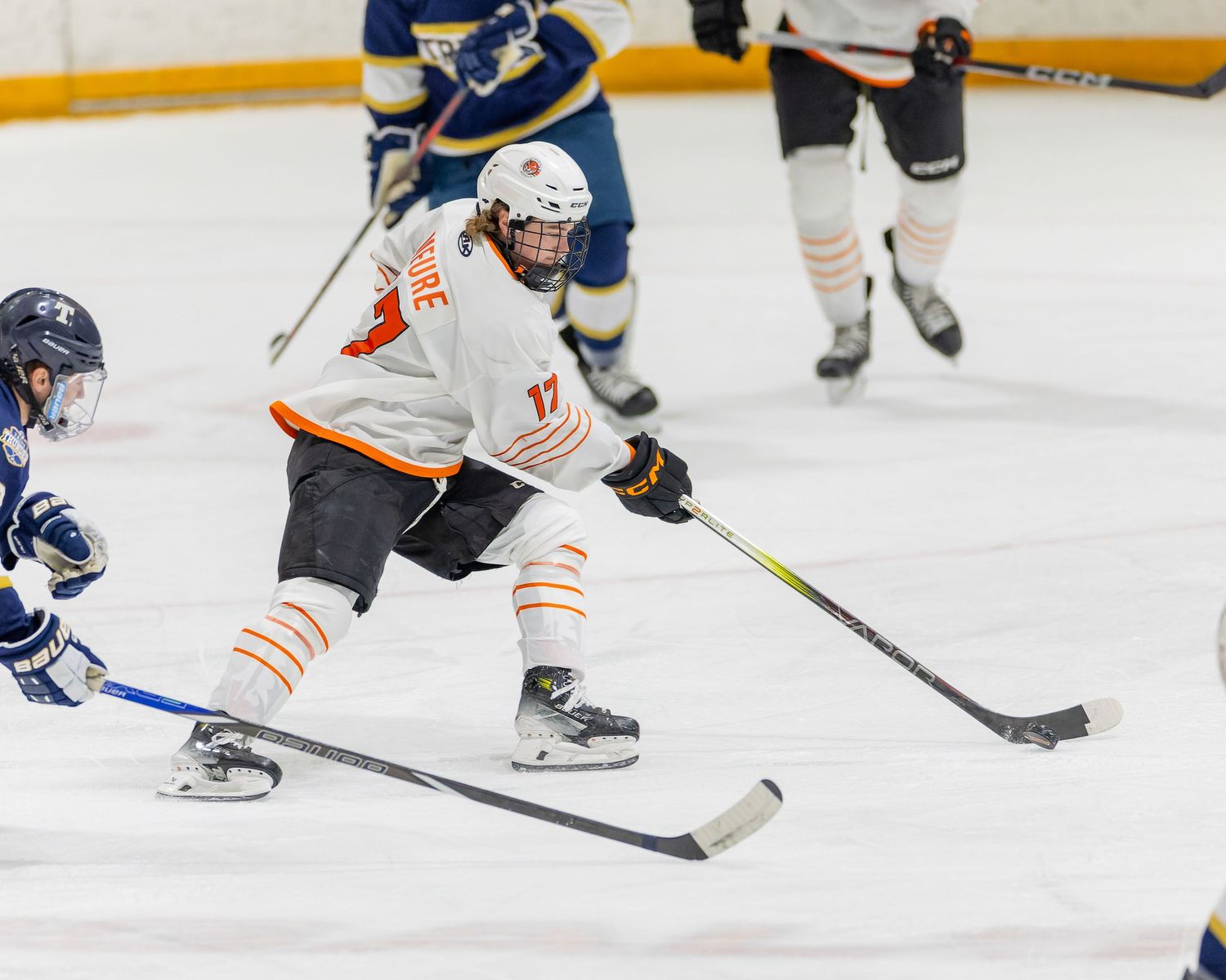 Youth hockey player in white jersey handles puck during competitive game against blue team opponent.