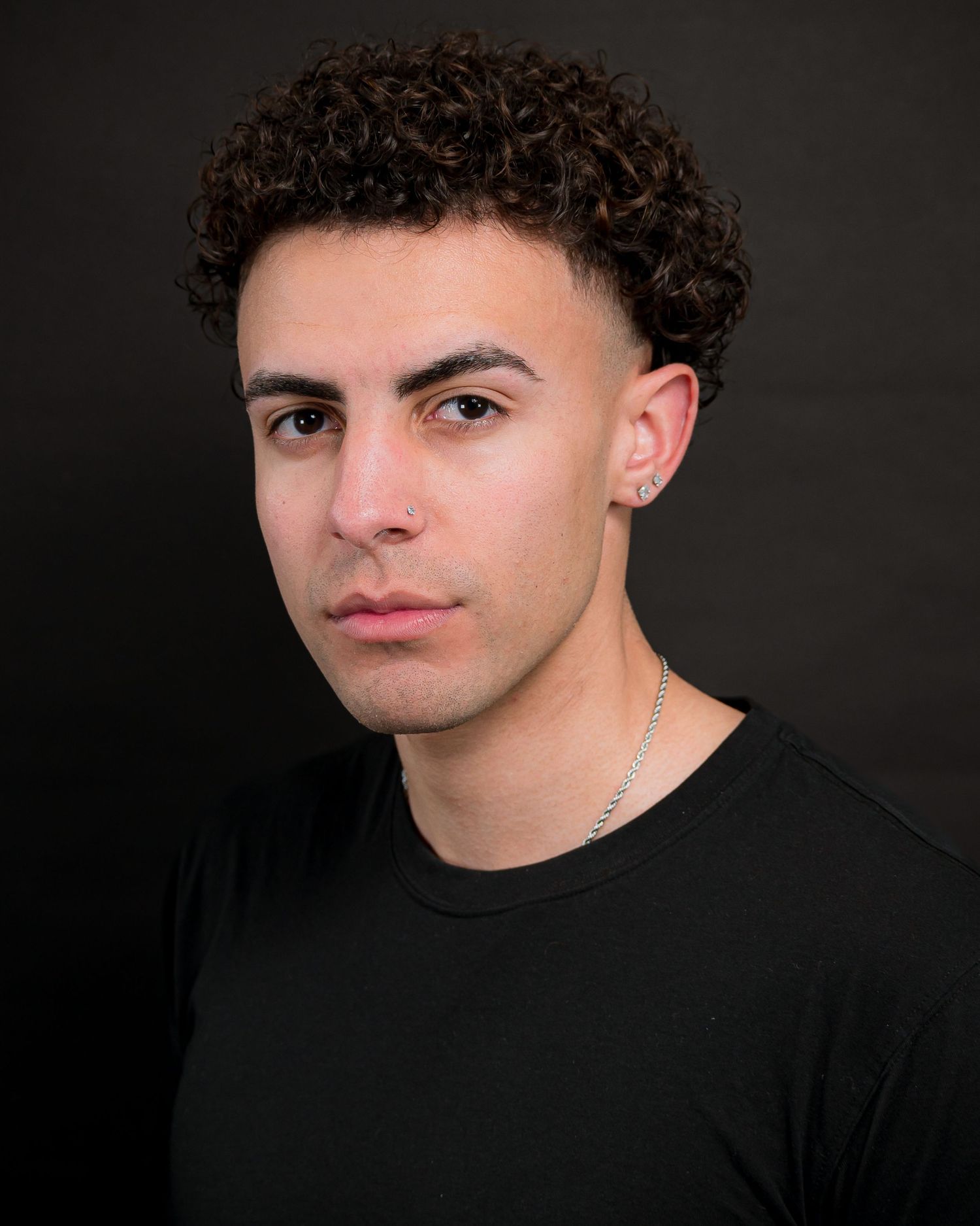Studio portrait with curly hair wearing black shirt against dark background.