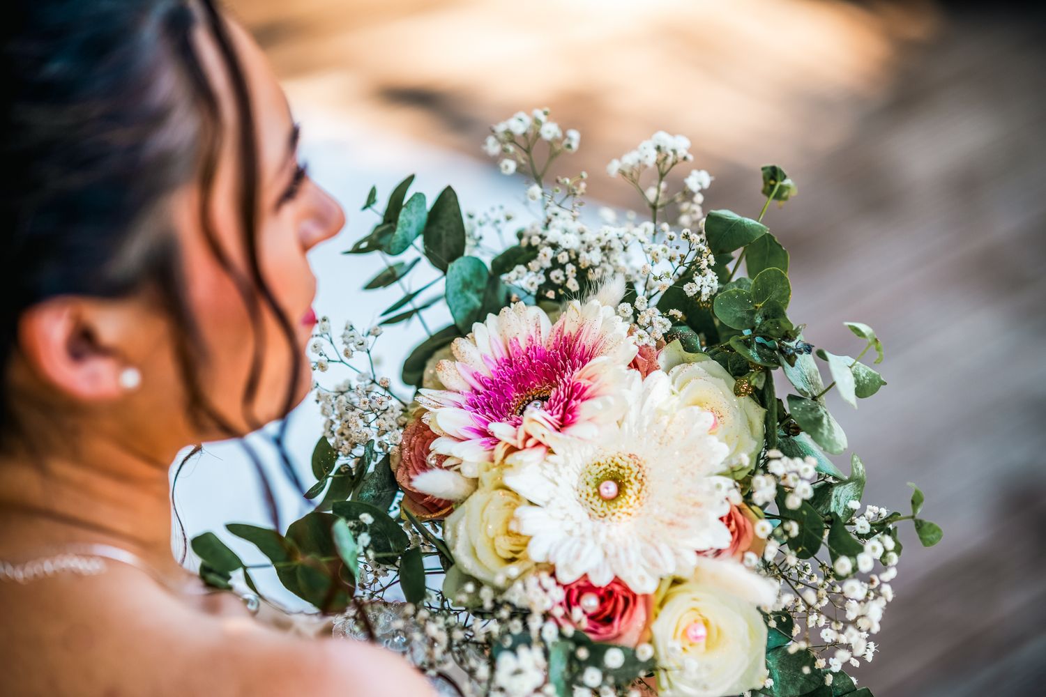 A colorful bridal bouquet with white and pink gerbera daisies, roses, and baby's breath flowers against a blurred background.