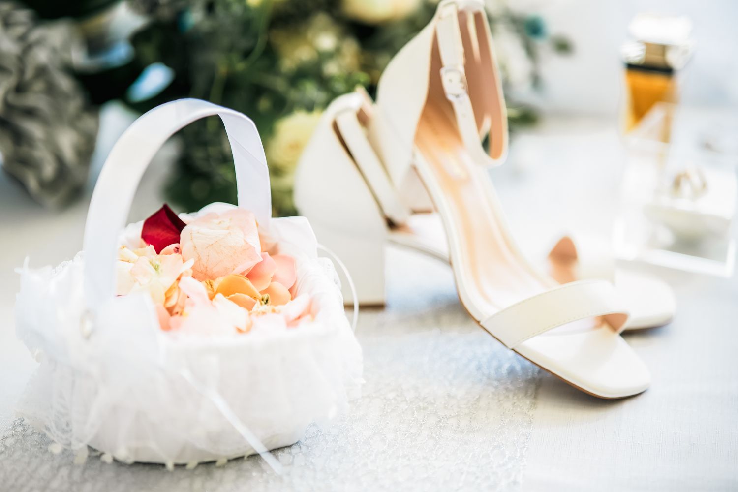White wedding flower basket and elegant ivory bridal heels arranged on light surface with soft romantic styling.