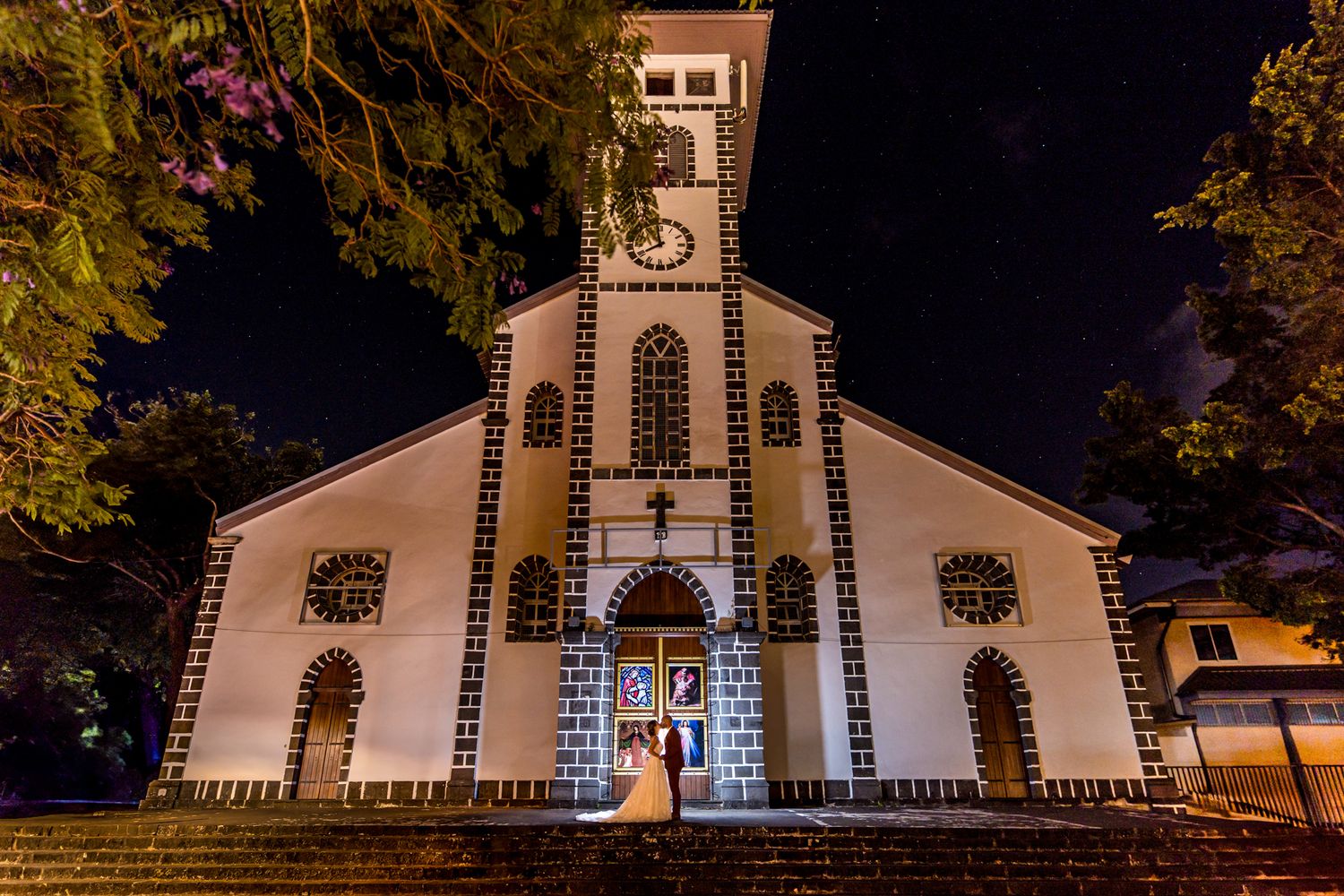 Illuminated white church facade with arched windows and clock tower photographed at night.