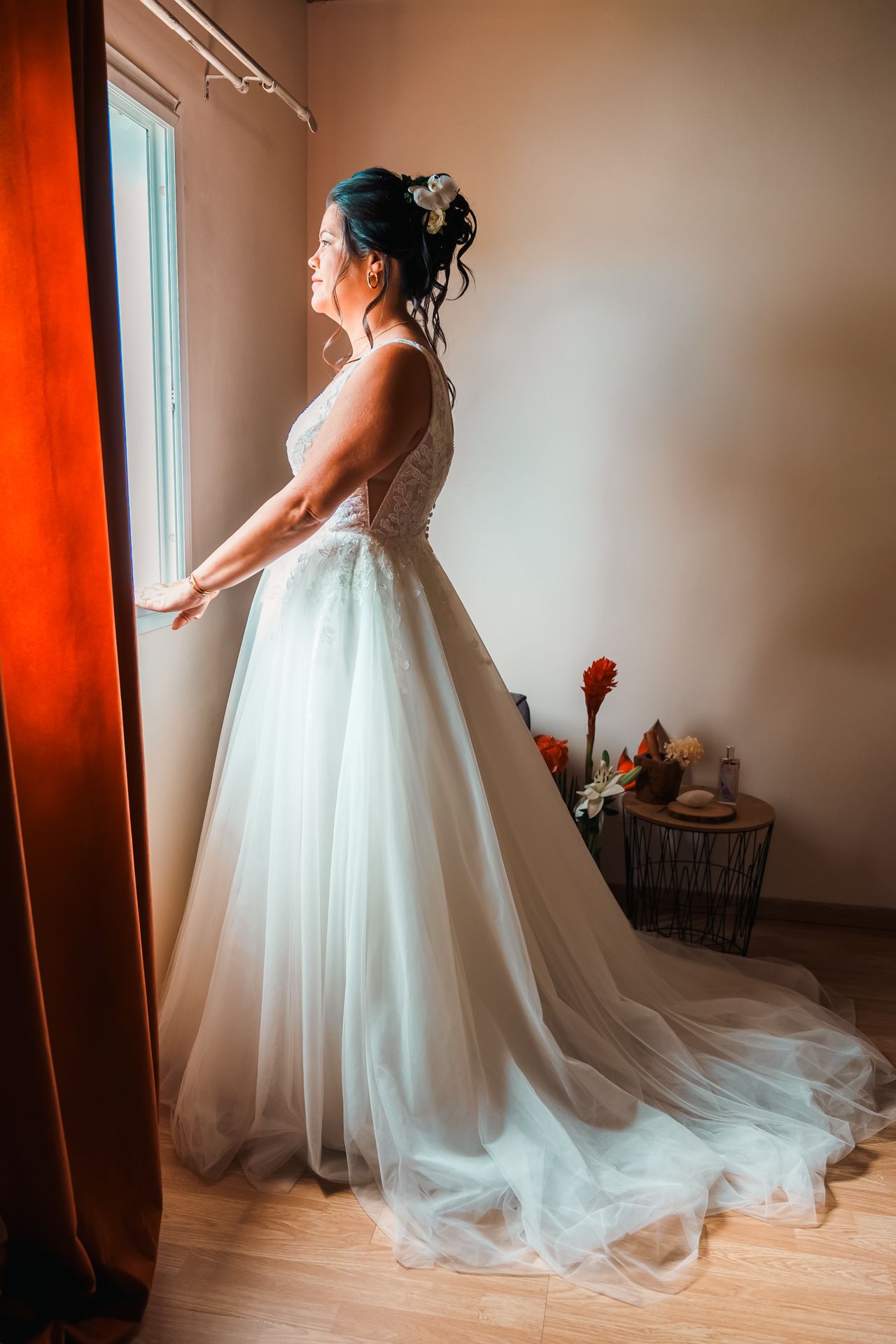Elegant white wedding dress with flowing tulle skirt and train captured in dramatic side profile near window.