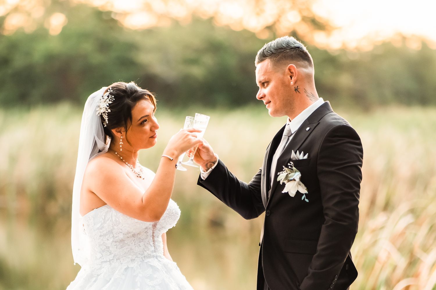 A bride and groom share a romantic moment in a sunlit field with golden grass during sunset.