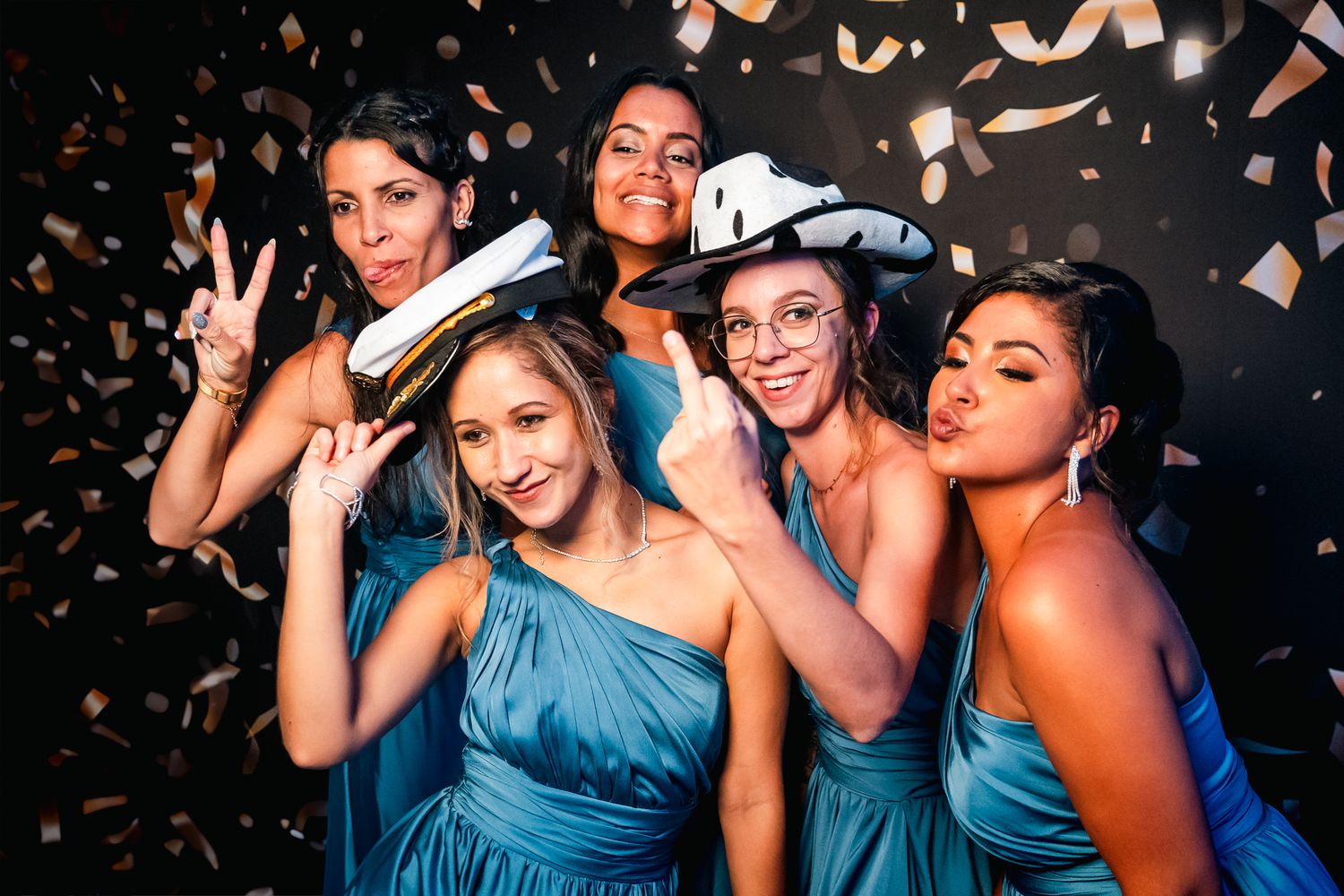 A group of bridesmaids in blue dresses pose playfully at a celebration with confetti falling around them.