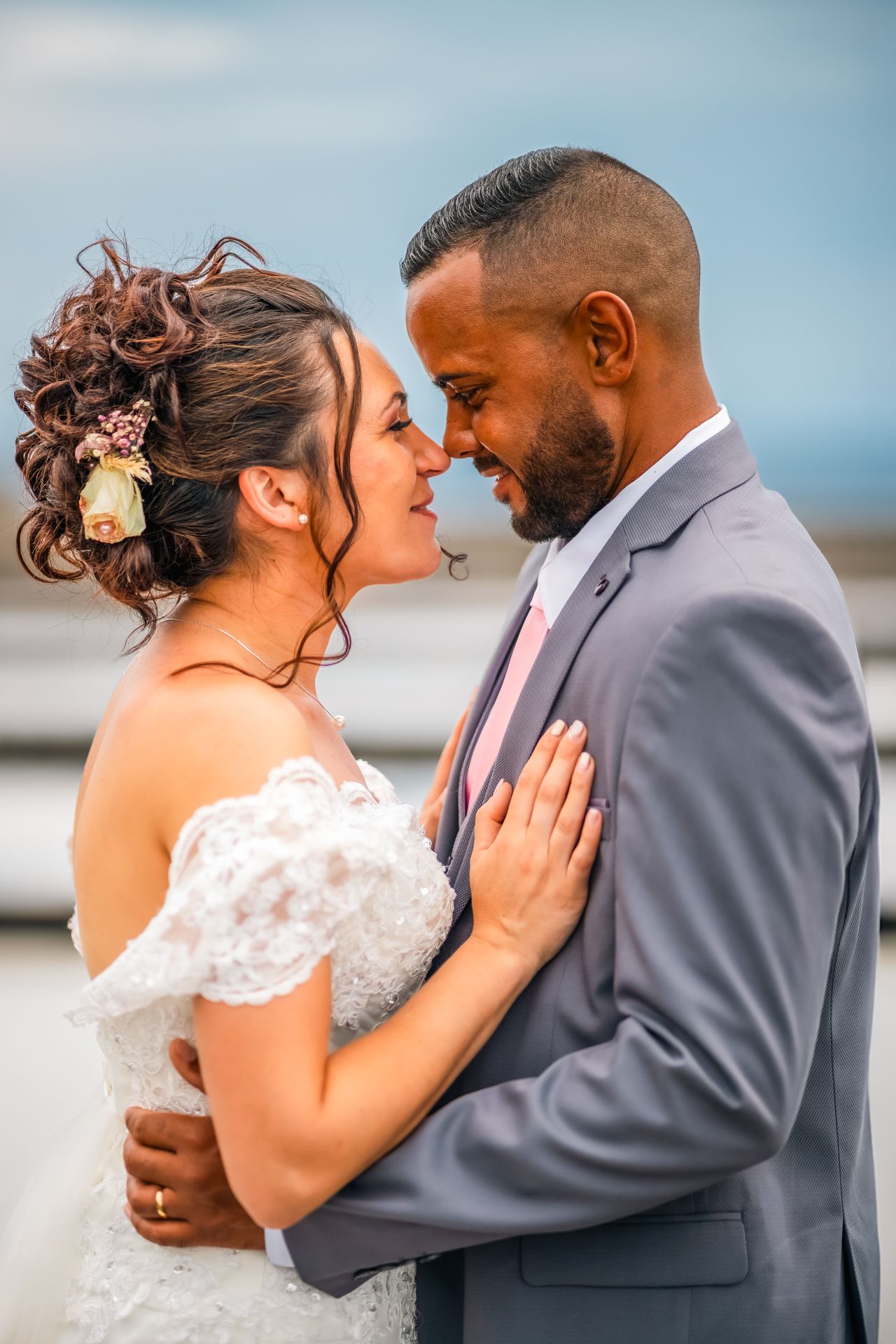 Newlyweds share an intimate moment together outdoors with the bride in white lace and groom in gray suit.