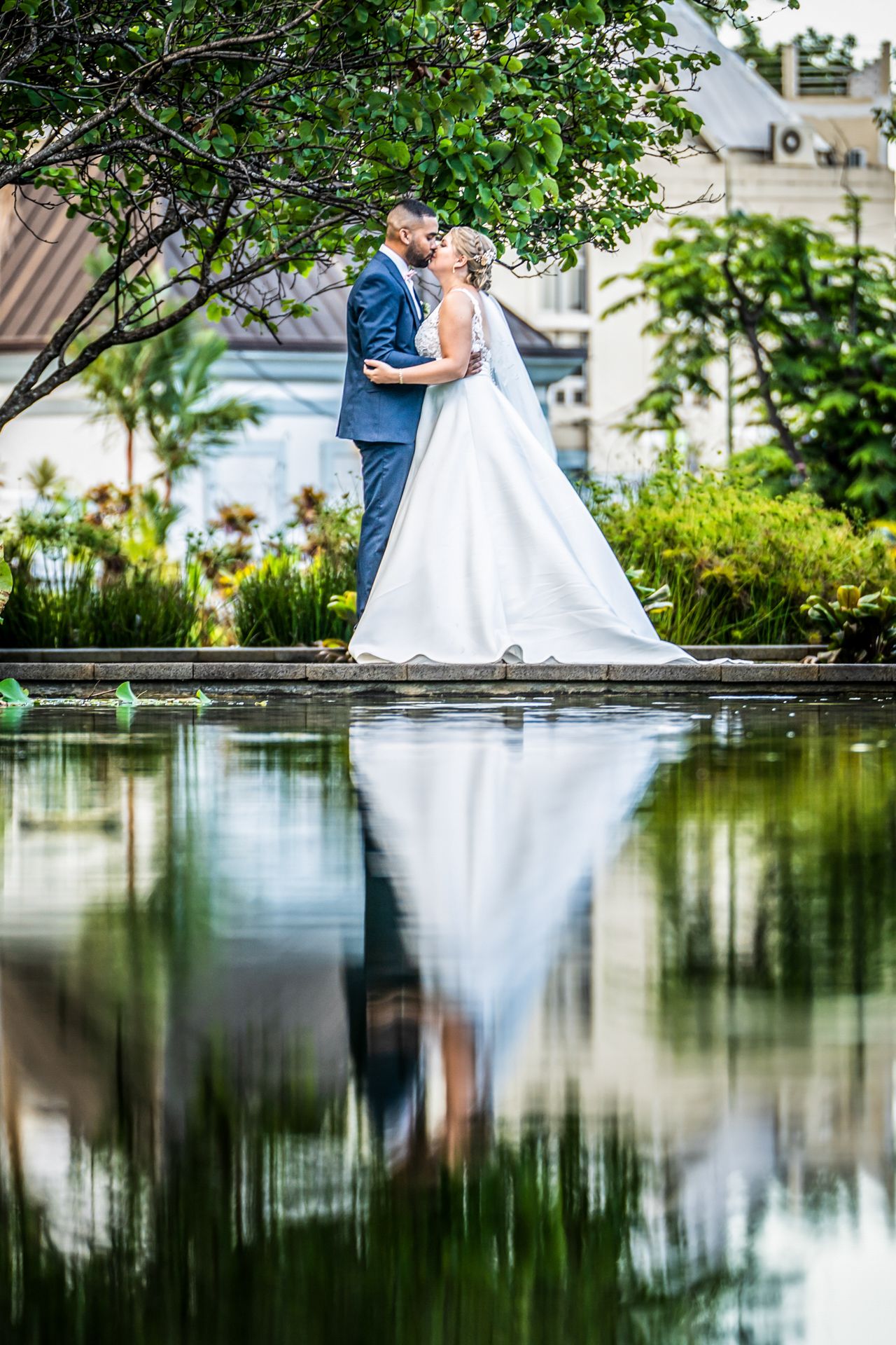 Beautiful wedding photo reflection in a serene pond surrounded by lush greenery and gardens.