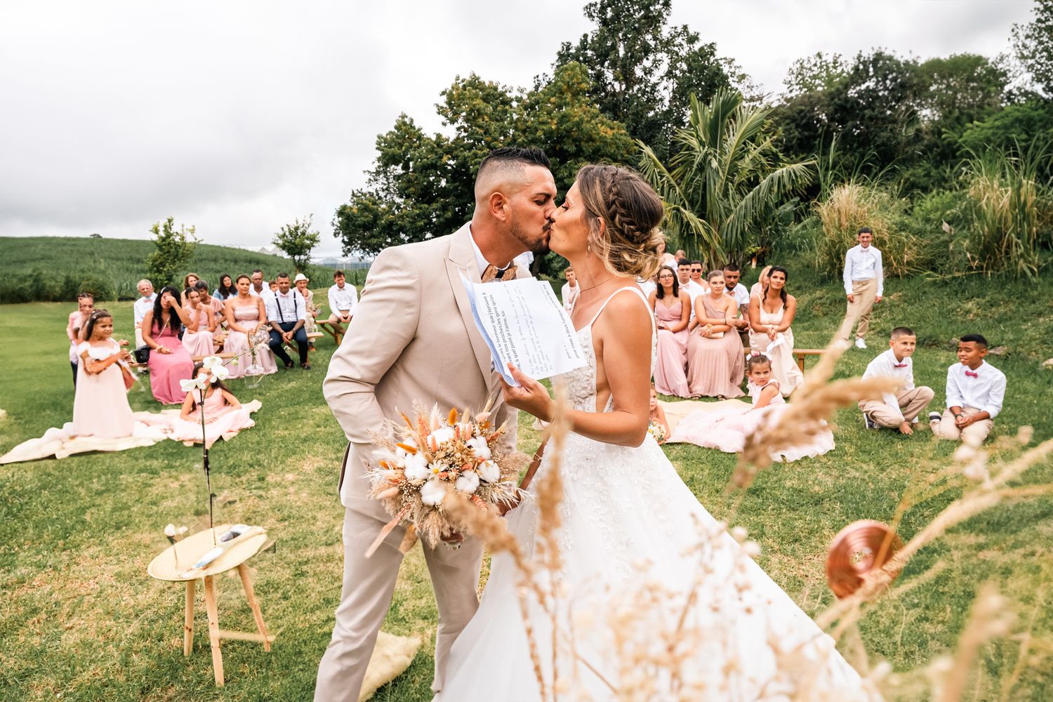 Wedding celebration outdoors with guests in pink dresses throwing confetti at the happy couple on a grassy field.