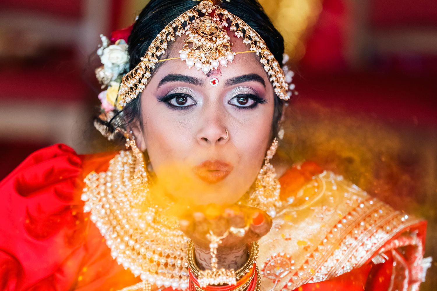 Traditional Indian bride wearing ornate gold jewelry and pearl accessories with dramatic eye makeup in red attire.