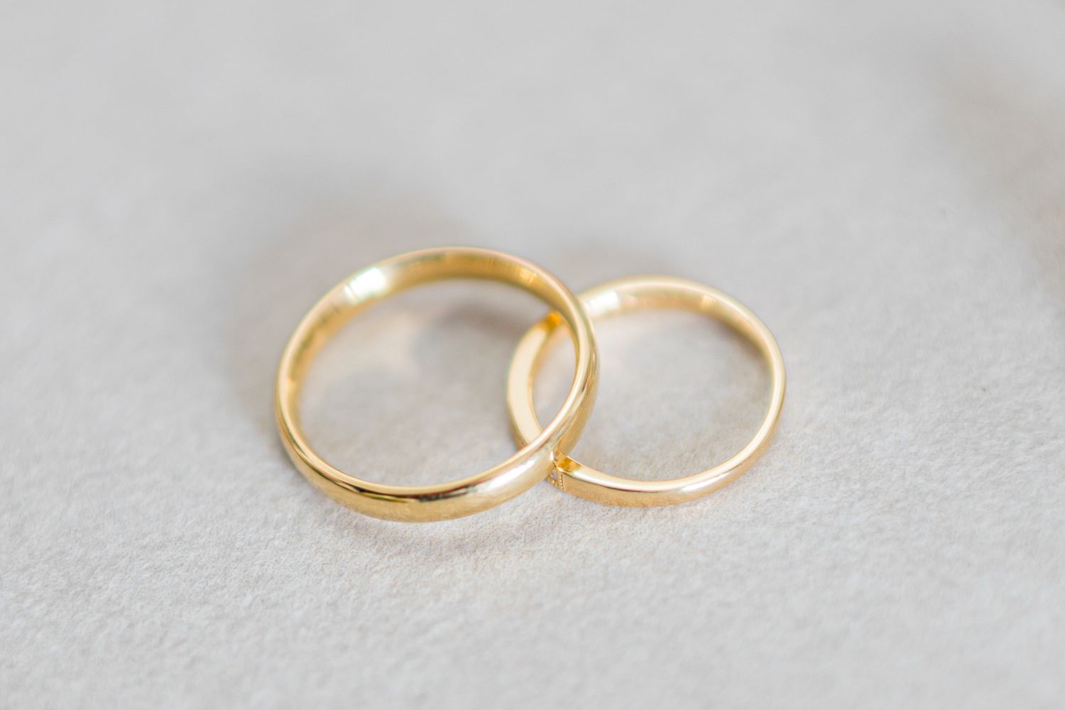 Two simple gold wedding bands of different sizes rest together on a light gray textured surface.