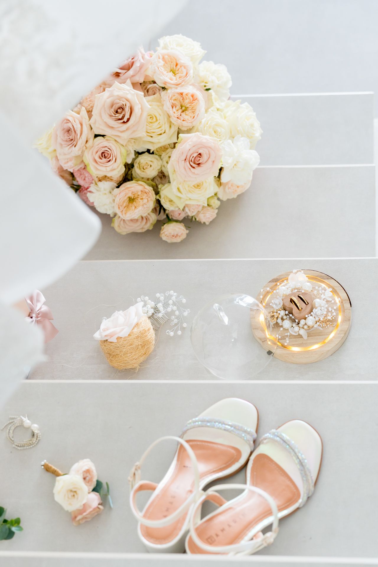 Wedding flat lay with pink and white roses, delicate accessories, and white strappy sandals.