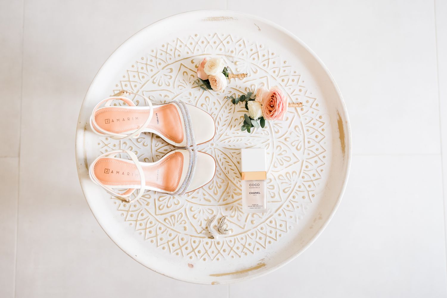 Blush wedding shoes and flowers arranged on a decorative white lace plate viewed from above.