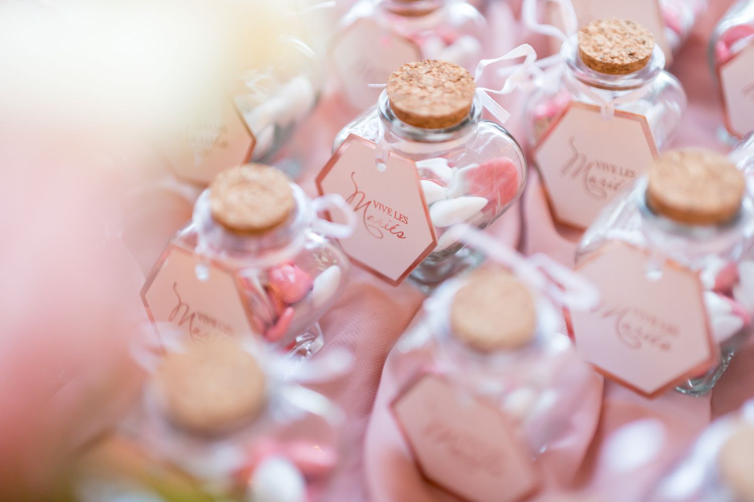 Small hexagonal glass bottles with cork stoppers filled with pink liquid for wedding favors or party decorations.