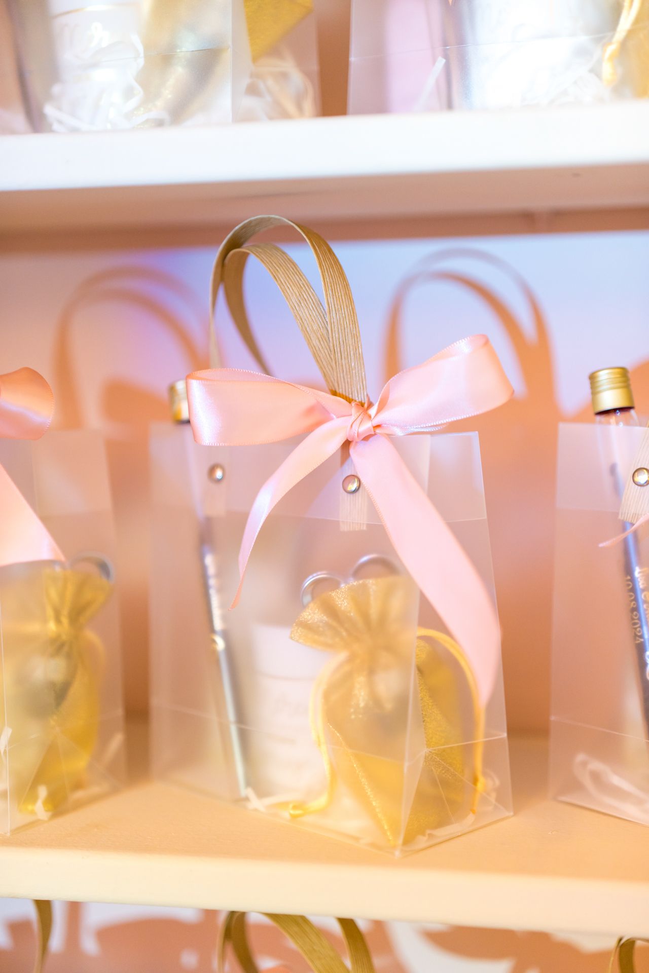 Clear favor bag decorated with pink satin bow and yellow organza pouch displayed on white shelf.