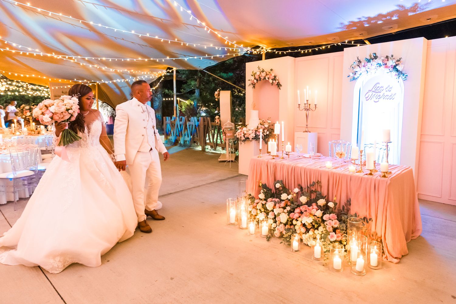 A dreamy wedding reception setup under twinkling lights with elegant decor, candles and floral arrangements adorning the space.