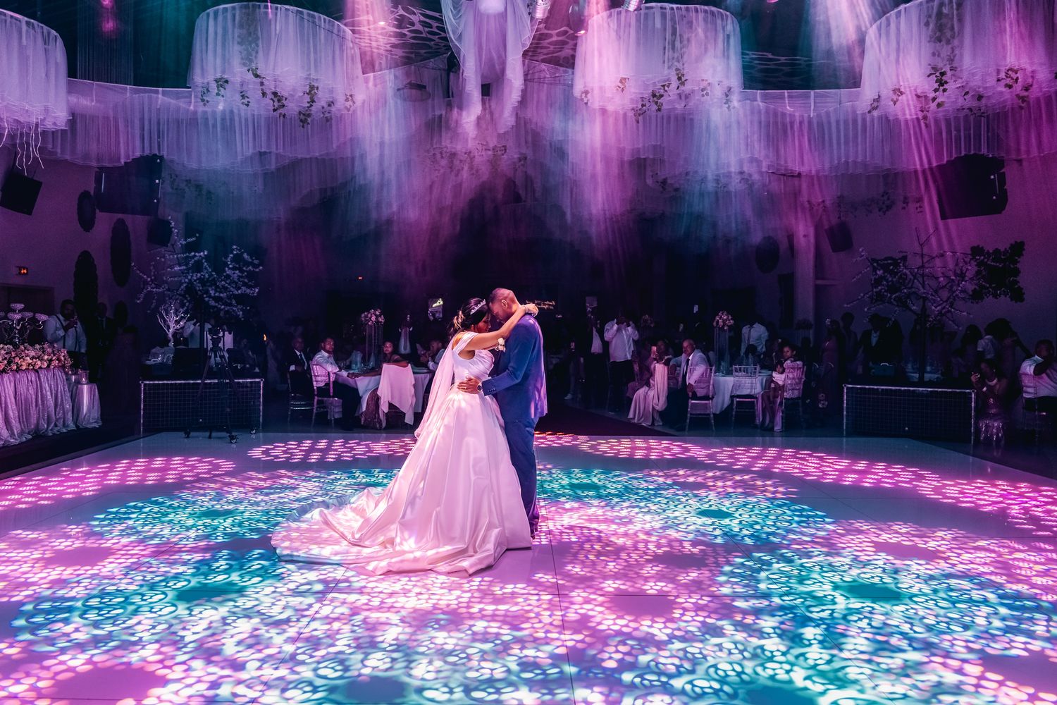 Couple dancing at a wedding reception with purple lighting and illuminated floor projections creating a magical atmosphere.