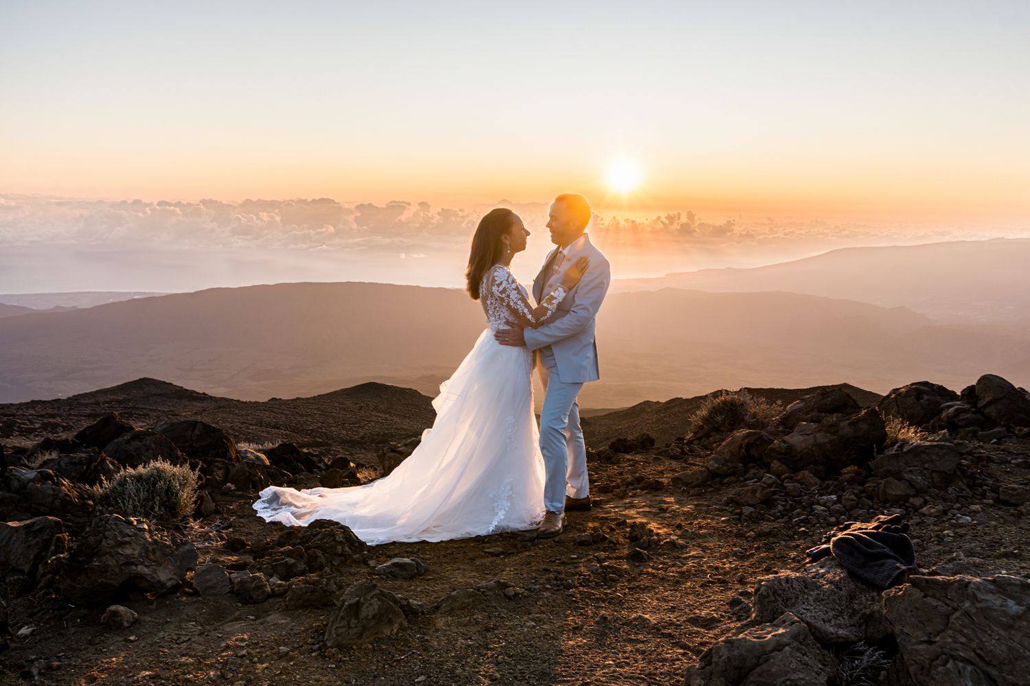 A couple shares an intimate moment on a mountaintop during golden hour sunset with misty mountains in the background.