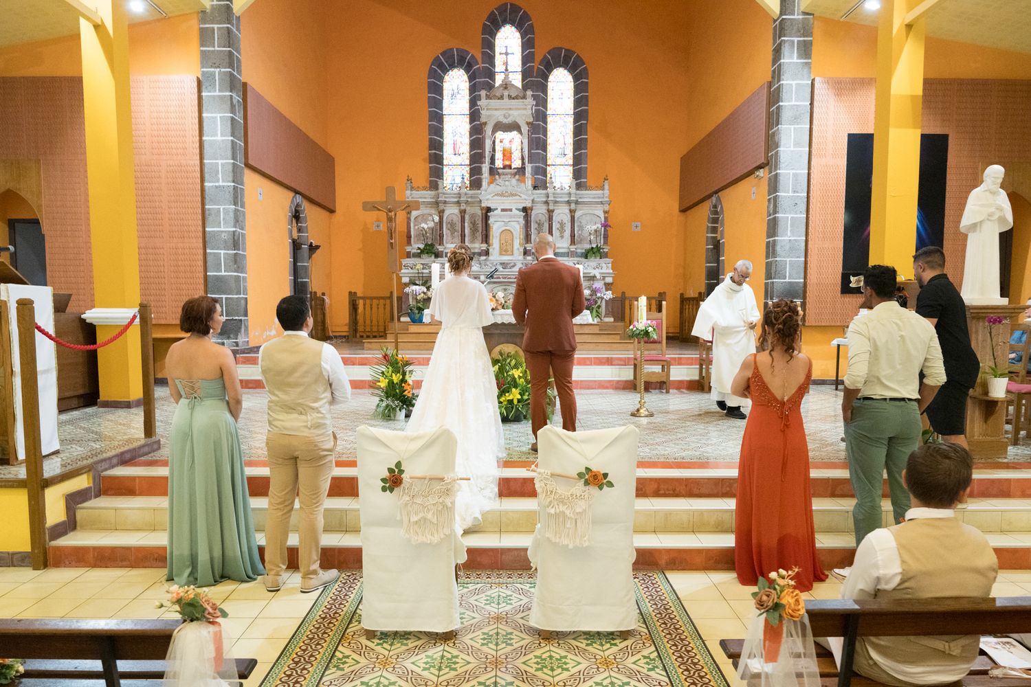 Interior view of a Catholic church wedding ceremony with guests in colorful formal attire gathered at the altar.