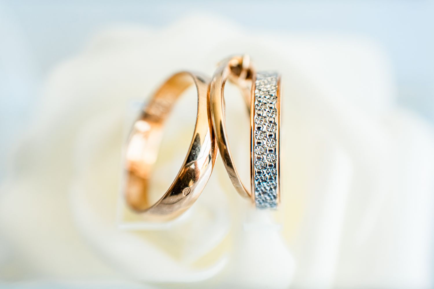 Two elegant wedding rings in rose gold, one plain band and one with sparkling diamonds, resting on a white surface.