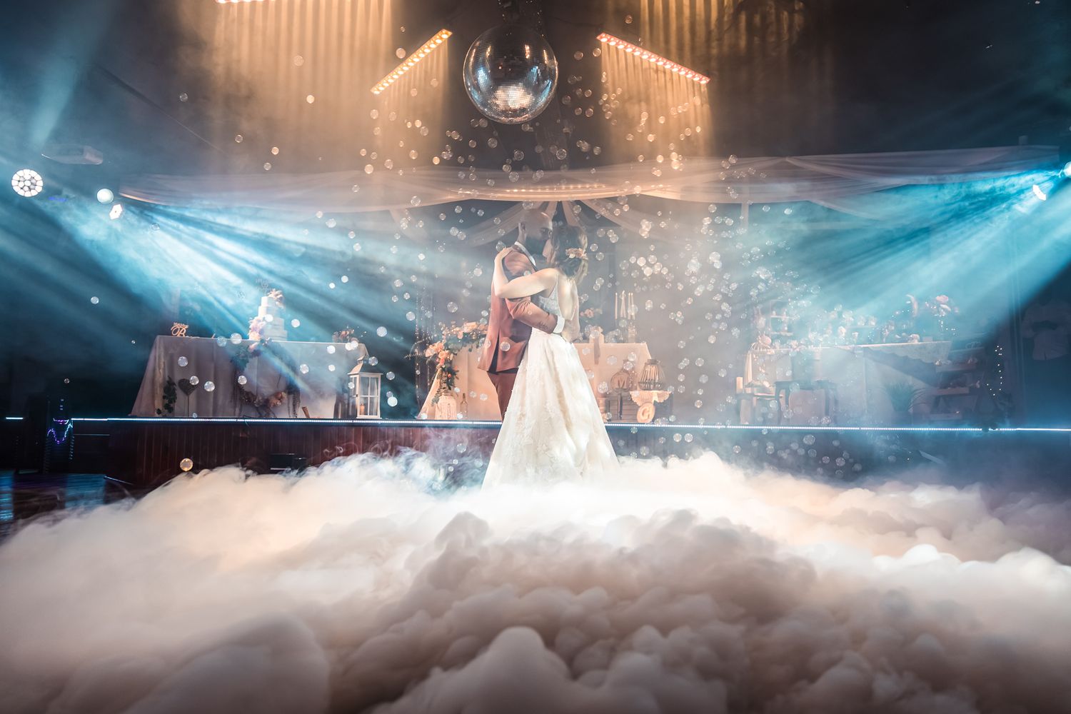 A misty dance floor illuminated by dramatic blue stage lighting creates a magical wedding scene.