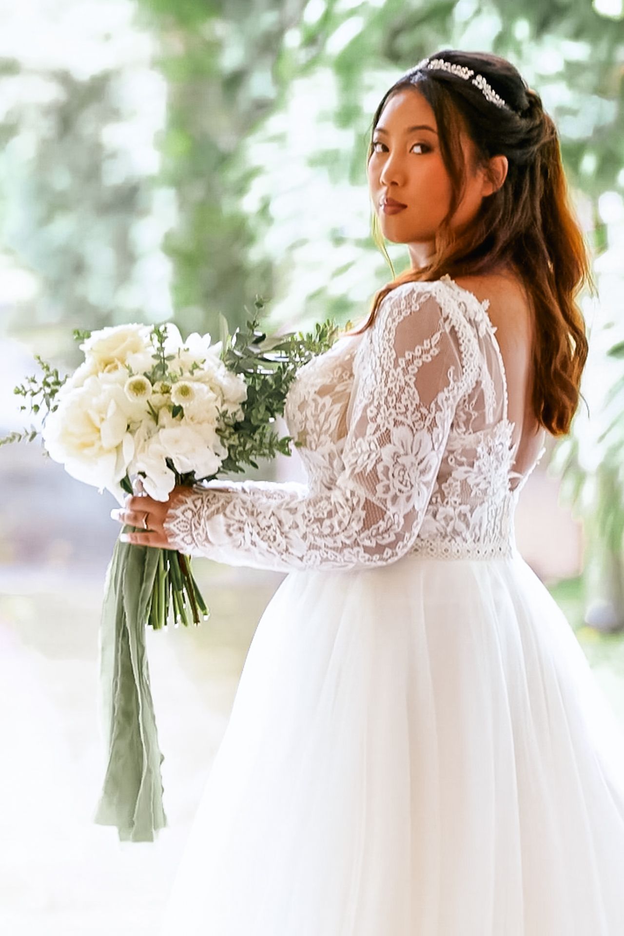 Side view of bride in long sleeve lace wedding dress holding white floral bouquet during outdoor portrait session.
