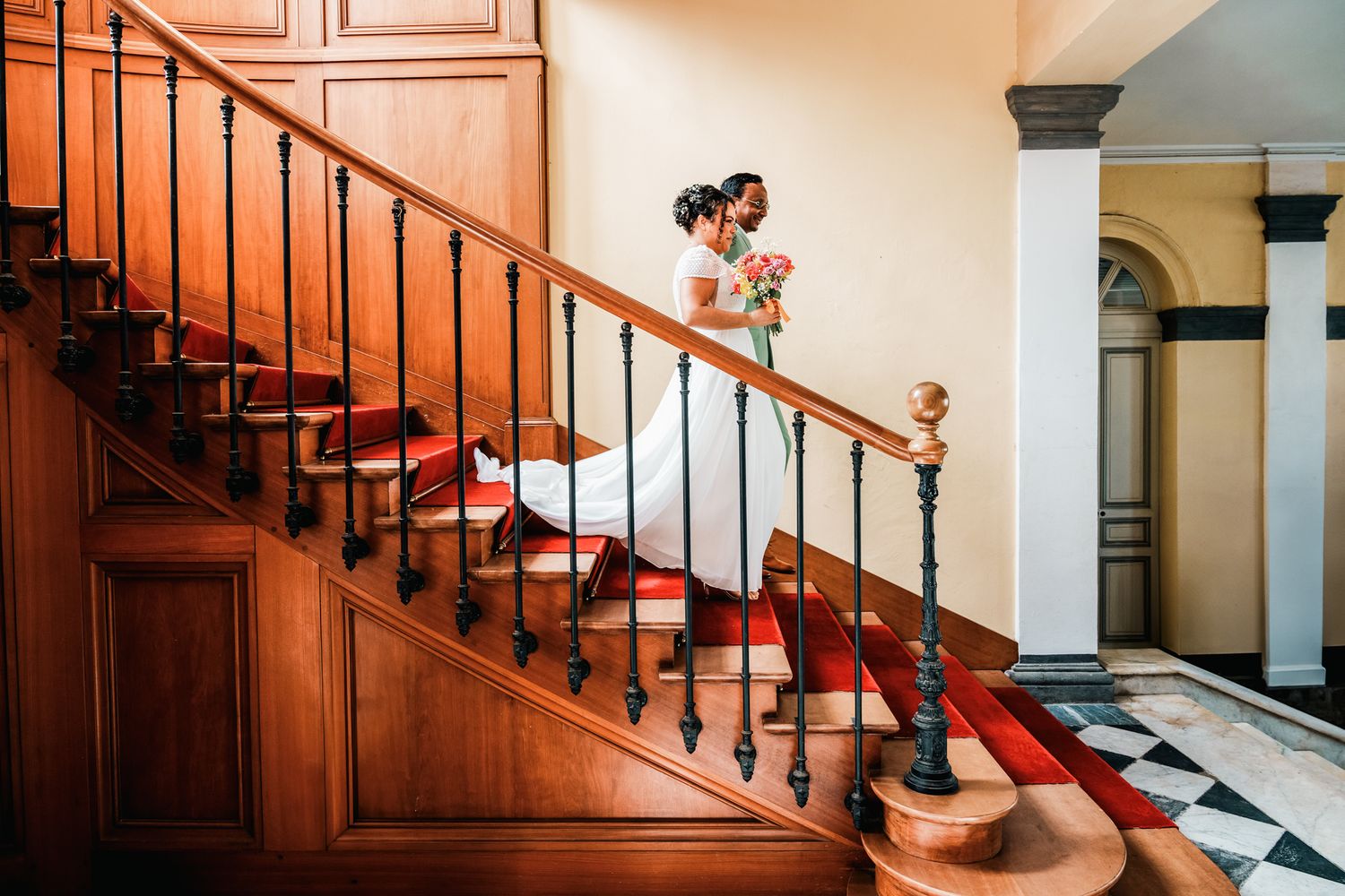 Elegant wooden staircase with red carpet runner and ornate balustrade in historic building interior.