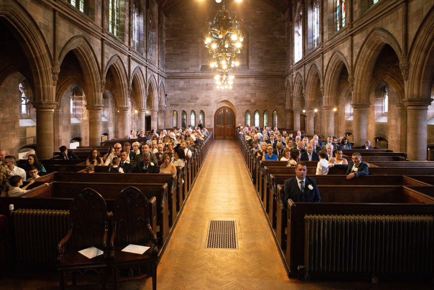 Interior of grand cathedral with wooden pews and glowing chandeliers.