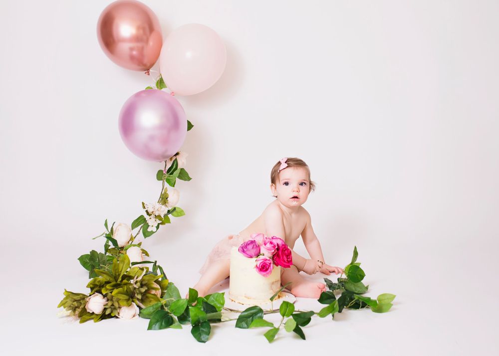 Studio setup with metallic balloons, pink roses, and green vine decorations against white backdrop.