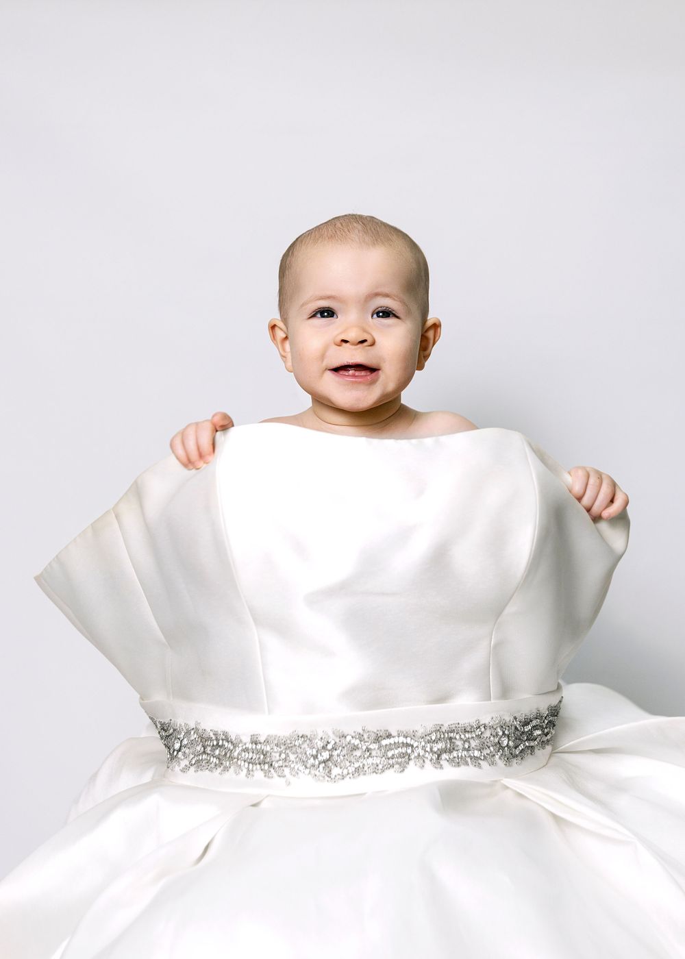 Baby peeking over white dress with sparkly belt detail.