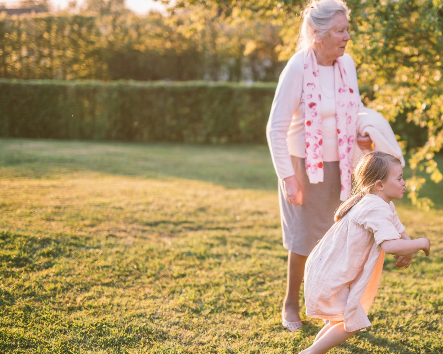 Sunlit garden scene during golden hour with figures enjoying outdoor activities.