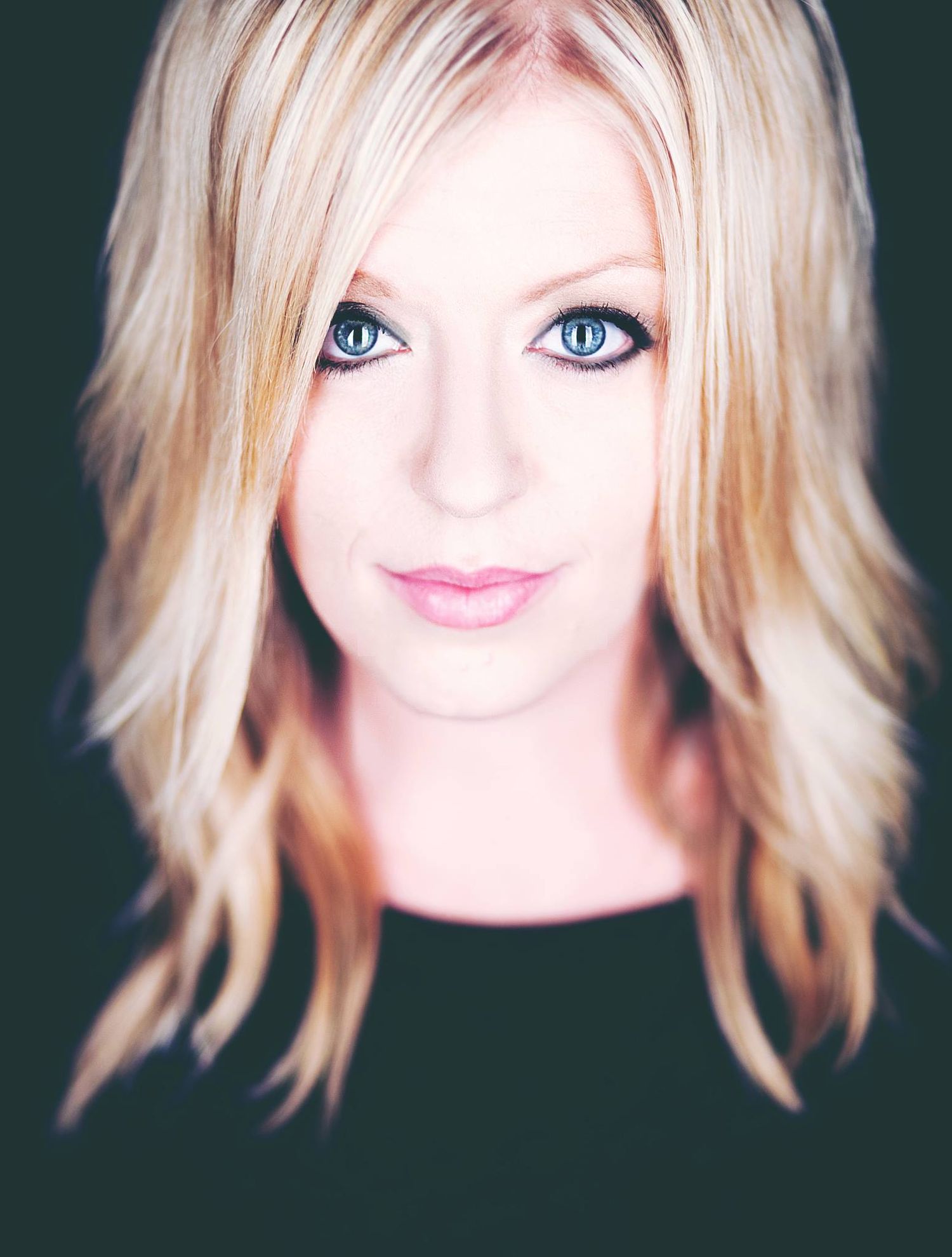 Studio portrait with dramatic lighting against dark background showing blonde layered hairstyle.