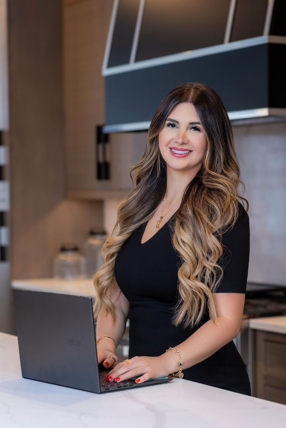 Professional working at desk in modern office with laptop wearing black outfit and long wavy hair.